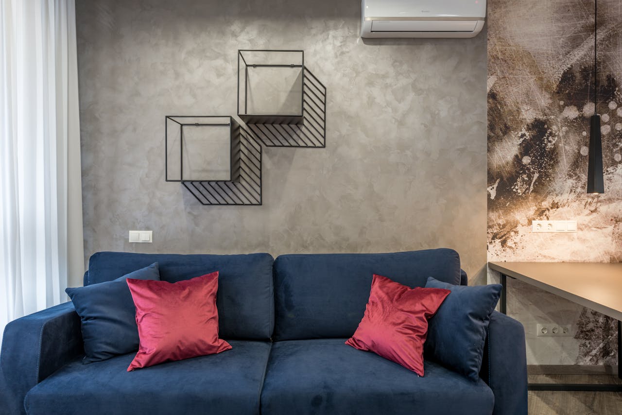 Comfortable soft sofa with pillows placed in modern living room near wall with creative geometric shelves